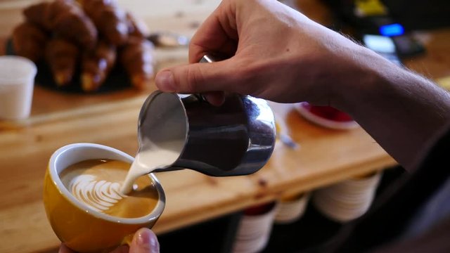 Barista draws milk over a coffee - making latte art for cappuccino