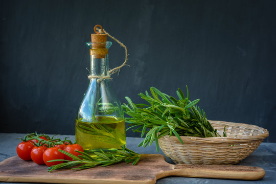 Fresh bunch of rosemary, cherry tomatoes with a bottle of rosemary oil or olive oil on cutting board over stone background.
