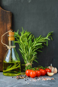 Fresh bouquet of rosemary, cherry tomatoes, garlic, spice and a bottle of rosemary oil or olive oil on a gray stone background.