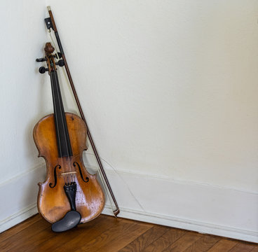 Vintage Violin With Broken String And Bow Leaning In Corner On Wood Floor