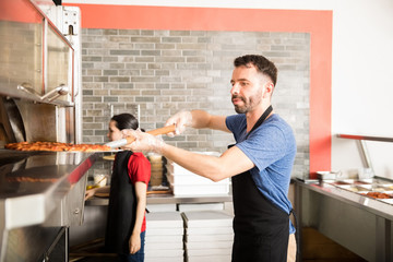 Restaurant chef removing freshly baked pizza out of oven - obrazy, fototapety, plakaty