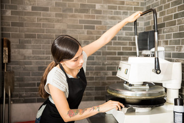 Young chef using dough press machine to make pizza
