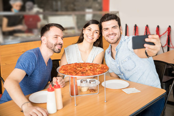 Young man taking selfie with friends having pizza