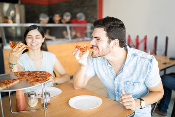 Handsome latin man enjoying eating pizza slice in pizza shop