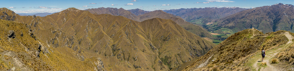 Panoramic view of the mountain range and a hiker trekking up Roy's Peak track on the south island of New Zealand
