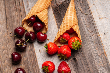 Fresh strawberries and cherries in waffle cones on wooden table