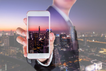Double exposure of businessman hold and show smartphone display and cityscape in the night as business, technology, communication and advertising concept.