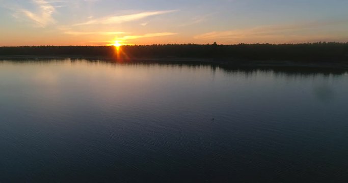 Sunset at a&acute;calm sea, C4K aerial rising view above reflecting, clear and low waters of the gulf of finland, on a sunny summer evening dusk, in Hanko, Finland