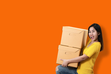 Portrait of young asian entrepreneur happy smiling and holding or carrying pile of boxes in hands on orange isolated background and copy space. Asian woman move to new home or ecommerce owner concept.