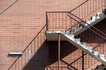 Concrete stairs with red metal railings against a red brick wall creating a strong diagonal shadow pattern