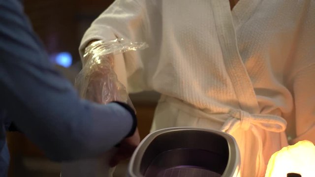 Closeup of a spa attendant wrapping a woman&rsquo;s hand in a plastic bag and then putting a glove on her as part of her paraffin skin treatment.