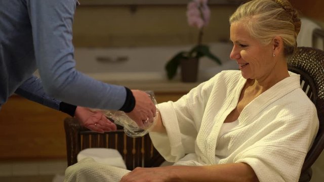 Closeup of a pretty mature blonde woman sitting in a chair in a spa and a therapist taking gloves off of her hands after having a paraffin wax treatment on her hands.
