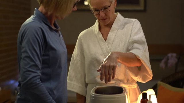 Camera sliding to the left of closeup of woman at a spa dipping her hands into hot paraffin for her skin treatment.