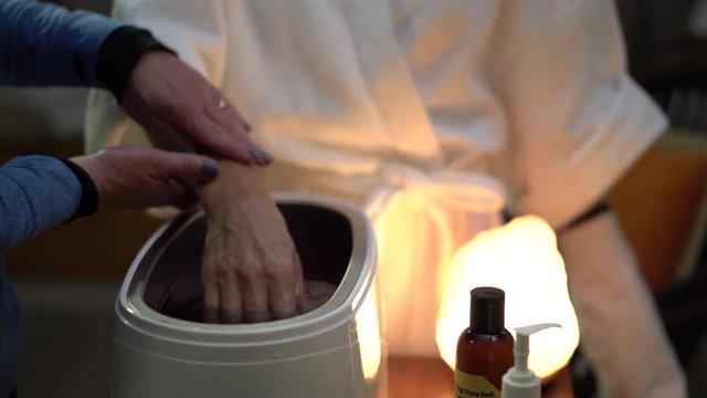 Closeup of an attendant, therapist dipping a woman&rsquo;s hand into hot paraffin wax.