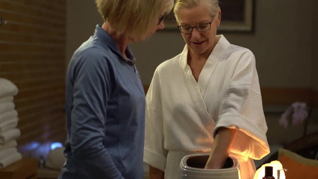 Camera sliding to the right of closeup of woman at a spa dipping her hands into hot paraffin for her skin treatment.