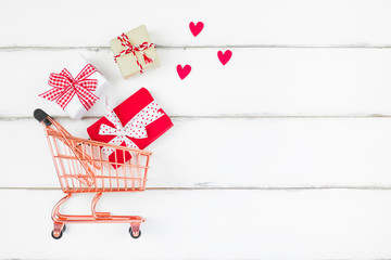 Art composition gifts box red ribbon, red heart and shopping cart on white wooden background with...