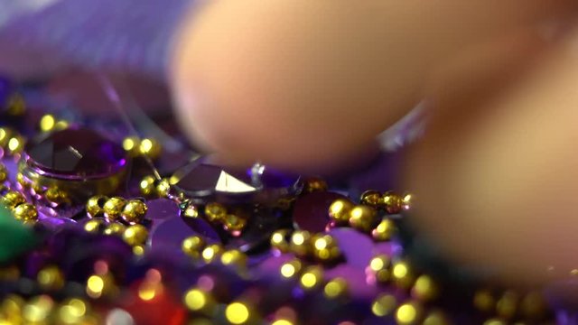 Camera follows the tip of a glue gun as it puts a glob of glue onto a costume, jewel is pressed into place, and glue gun tip puts more glue in another spot.