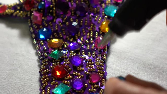 Closeup of a woman&rsquo;s bra decorated with jewels and a glue gun putting hot glue on and a finger pressing a rhinestone into the glue.
