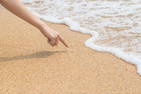 Woman's finger is drawing on beach sand