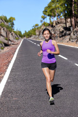 Running runner woman athlete jogging on nature road in mountains training cardio for marathon run breathing and doing endurance workout. Happy Asian girl working out outside in summer.