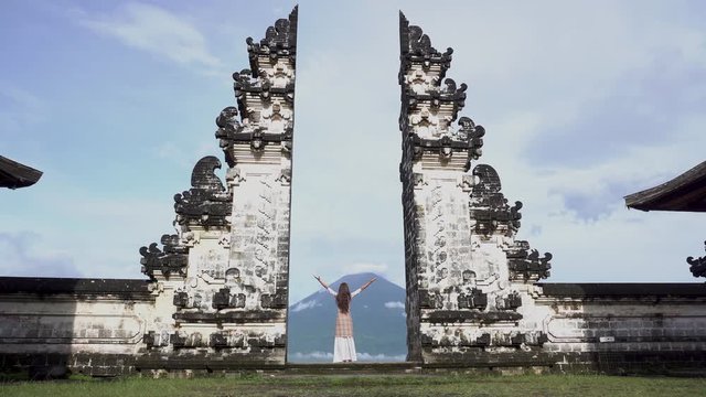 Woman with arms wide open standing in temple gate, looking at Agung volcano.