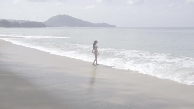 A woman is standing by the sea and looking out of the horizon. S-log, ungraded, no color.