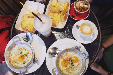 Typical breakfast with fried egg or pan omelet,Garlic bread and herb bread slice in white plate and Fried Fish balls with tomato sauce and cups of coffee on the table.