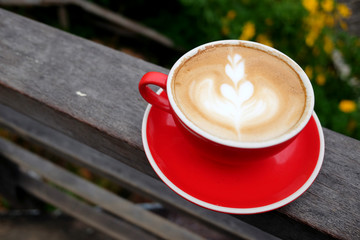 A red cup of coffee on the fence of terrace in nature with mountain and flowers field background.