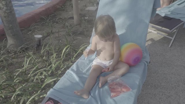 Baby at the pool eating a watermelon on a deckchair. S-log, ungraded