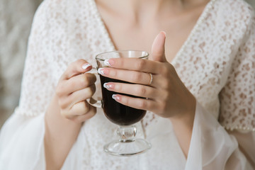 The bride is holding in her hands with a beautiful manicure an espresso cup
