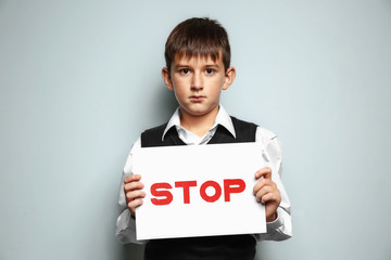 Little boy holding sign with word "Stop" on light background