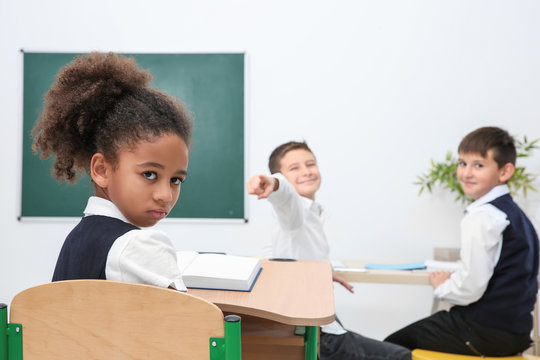 Children bullying African-American girl in classroom