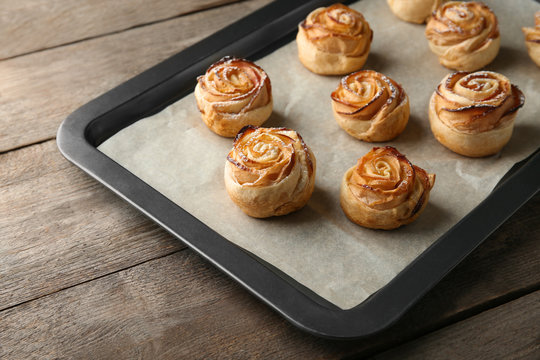 Baking tray with apple roses from puff pastry on wooden background