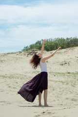 Fototapeta na wymiar Woman in a long dress is dancing on the sand