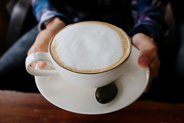 A young woman holding a white cup of coffee in her hands and drinking it in the morning