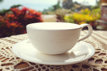 A white cup of hot coffee on wooden table in the garden of coffee shop