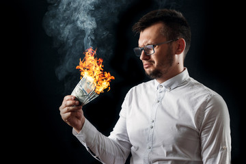 A man holds burning money in his hands, burning US dollars. The concept of inflation, a decrease in...