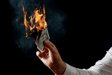 Male hand close-up, holds burning money in hands, burning US dollars. Black background, isolate....