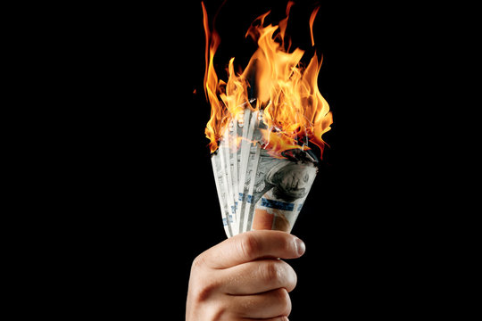 Male hand close-up, holds burning money in hands, burning US dollars. Black background, isolate. The concept of inflation, a decrease in the purchase of foreign currency, and devolution.