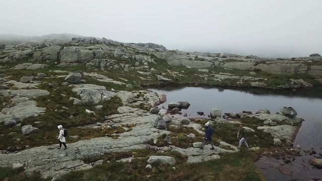Aerial shot of people hiking near a water pool in mountains on a cloudy day
