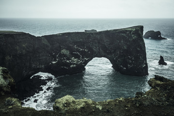 Fototapeta premium Abstract rock formations in the sea with two tunnels in the rocks and a green cliff as an edge between the sea and the rocks with a green foreground and a blue background in Iceland