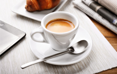 Espresso coffee and croissant on desk with tablet and newspapers