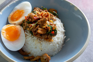 Spicy fried rice with stir fried duck with holy basil with boiled egg and lime in white round plate over wooden table.