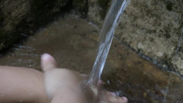 Close up of child's hand washing in runoff from natural spring water with rocky background