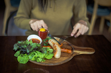 Blurred hand of Woman holding knife and fork for eating food, close up Sausage with Tomato Sauce and green vegetable on wood plate