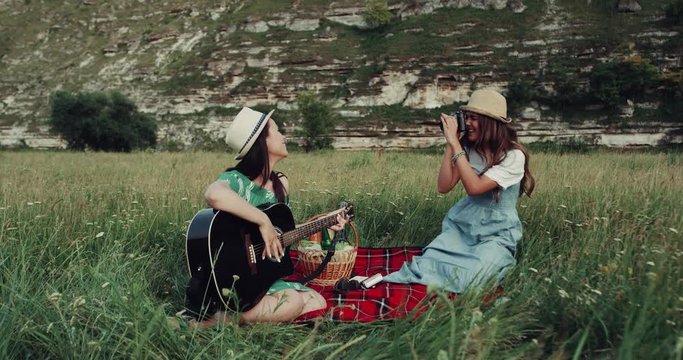 Two girls have picnic in the amazing place with mountains , they are singing at the guitar and taking amazing pictures. slow motions