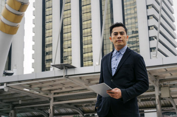 young handsome asian business man standing and working about finance on digital tablet in office building, technology, internet, investment, stock market and global business concept