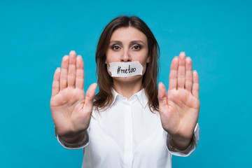 Young woman in an office white shirt with a mouth plastered with plaster and an inscription metoo,...