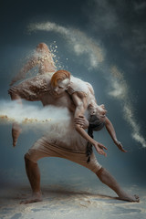 Dancing in flour concept. Guy male man and girl woman female dancers in dust / fog. Couple in love dancing and making dance element in flour cloud on isolated grey background