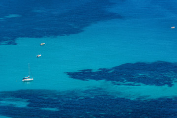 Fototapeta premium Aerial view of tropical turquoise blue sea with floating boats and people. High resolution image of sailing boats anchored next to reef around the coastline. Bird's eye view, ocean from above.